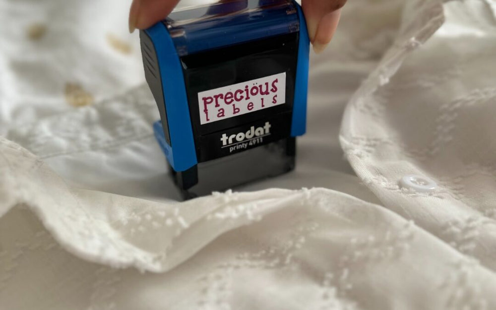 A Precious Labels self-inking Trodat name stamp being pressed onto a white cotton garment
