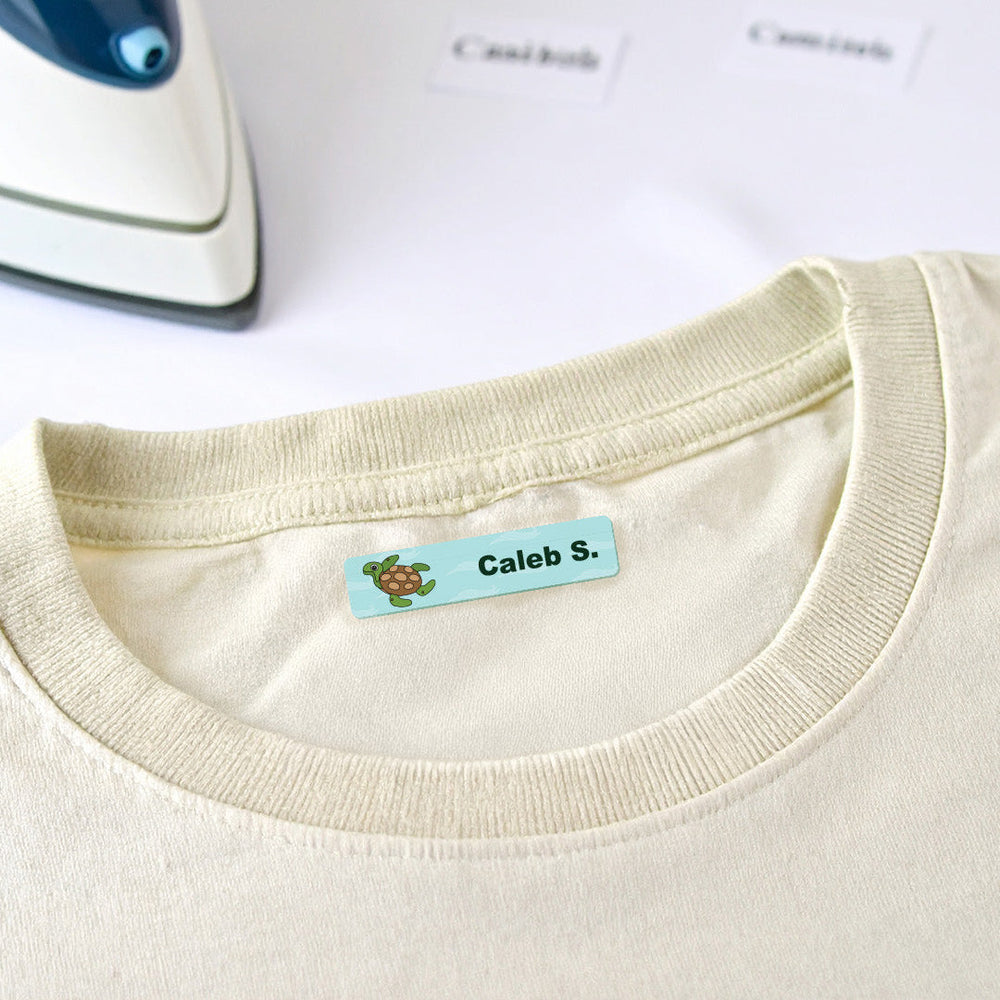 An iron resting beside a cream t-shirt with an iron-on name label on the inside collar
